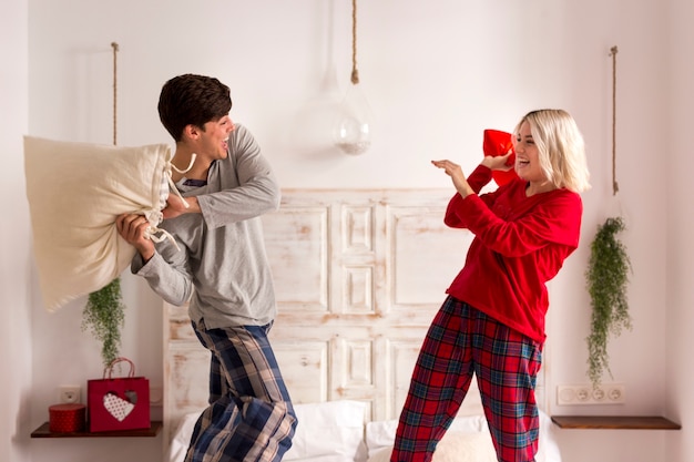 Homem e mulher tendo uma luta de almofadas no quarto