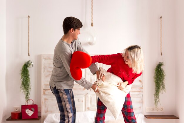 Homem e mulher tendo uma luta de almofadas no quarto