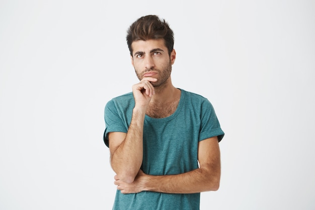 Homem elegante e elegante, com olhos escuros em roupas casuais, olhando de lado com olhar calmo e pensativo. Cara pensativa com expressão confusa, pensando em algo ou construindo planos