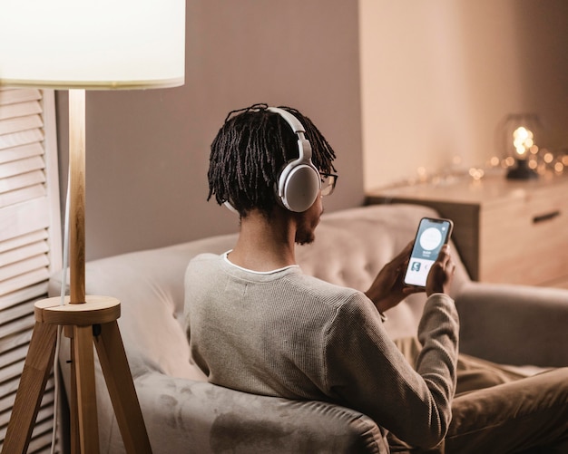 Foto grátis homem em casa no sofá usando smartphone e fones de ouvido