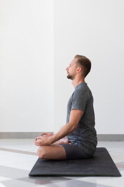 Homem em cena completa fazendo pose de sukhasana em ambiente fechado