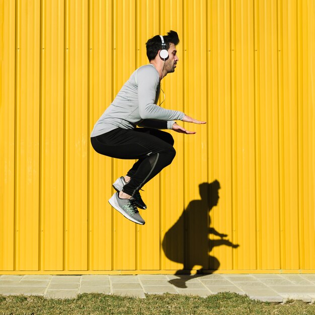 Homem em fones de ouvido pulando perto da parede amarela