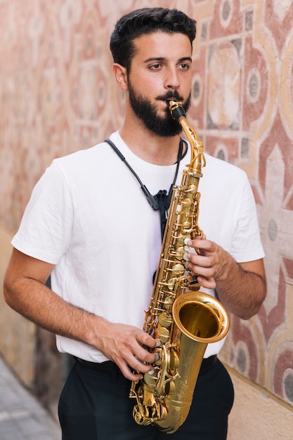 Foto grátis homem em pé tocando saxofone com fundo geométrico