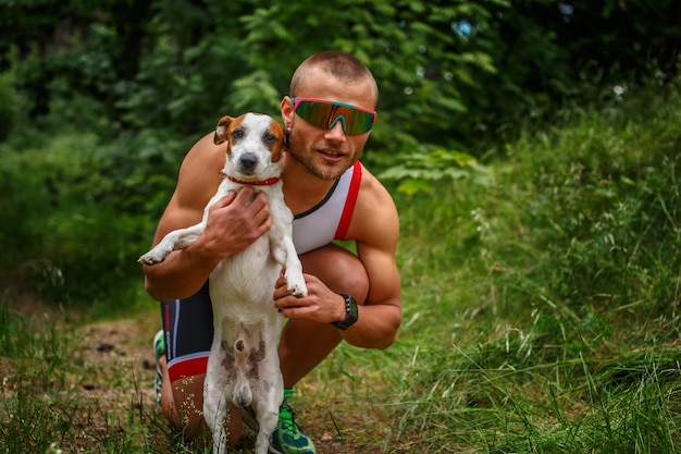 Homem em roupas esportivas e óculos de sol com seu cachorrinho fofo na floresta