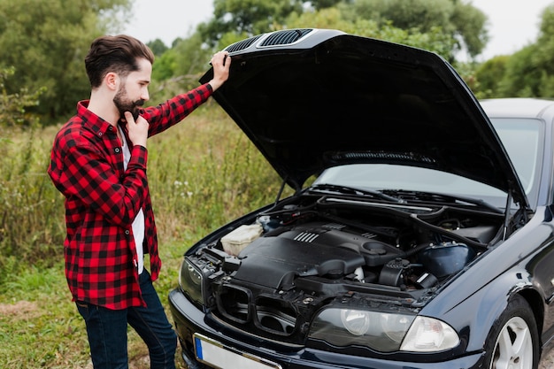 Homem encostado no capô do carro aberto