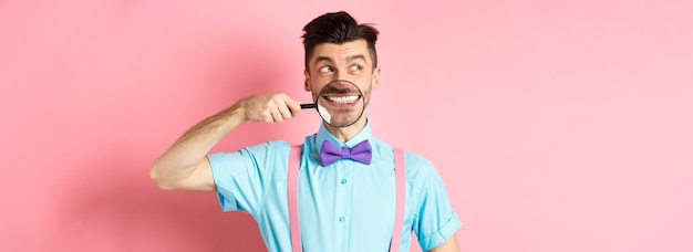 Homem engraçado em gravata borboleta sorrindo mostrando os dentes com lupa e olhando de lado para o logotipo em pé o