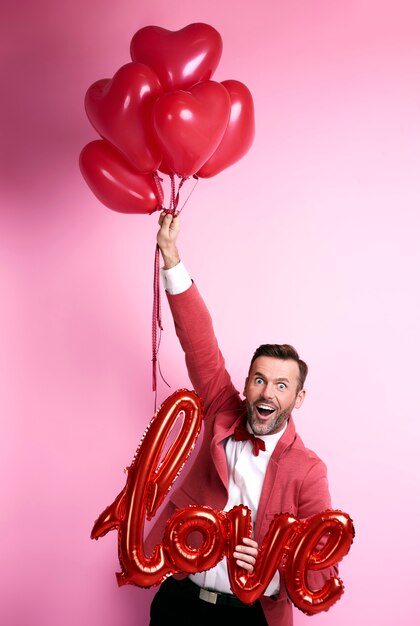 Homem engraçado segurando um monte de balões em formato de coração