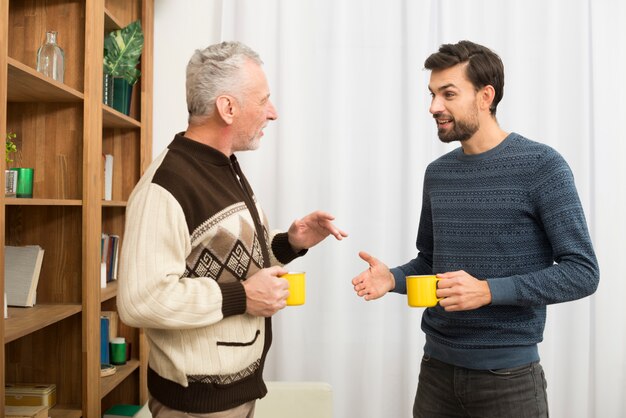 Homem envelhecido e rapaz com copos no quarto