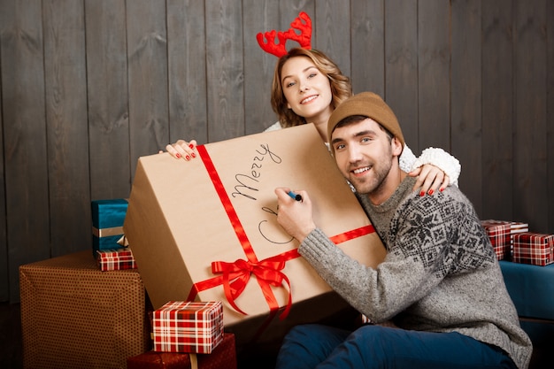 Homem escrevendo na caixa de presente feliz natal sentado com a namorada.