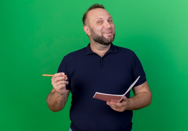 Homem eslavo adulto alegre segurando uma caneta e um bloco de notas, parecendo isolado