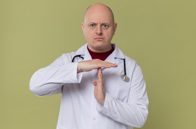 Homem eslavo adulto confiante com uniforme de médico e estetoscópio fazendo sinal de tempo limite