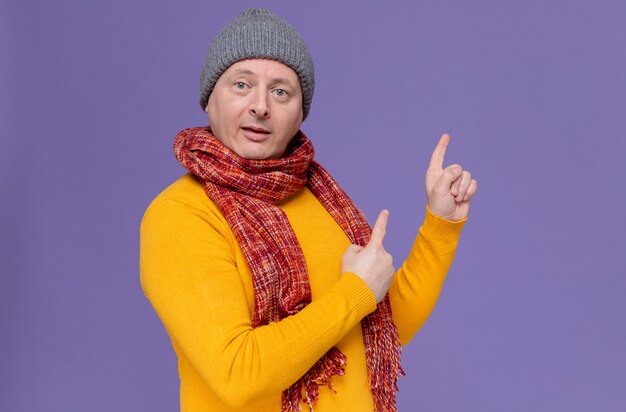 Homem eslavo adulto impressionado com chapéu de inverno e lenço no pescoço apontando para cima
