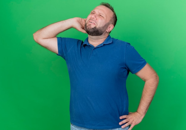 Homem eslavo adulto insatisfeito colocando as mãos na cintura e atrás da cabeça, olhando para o lado isolado na parede verde