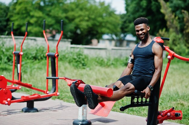 Homem esportivo de atleta masculino afro-americano com capa de braço esportivo para celular fazendo exercícios nos simuladores de treino de rua