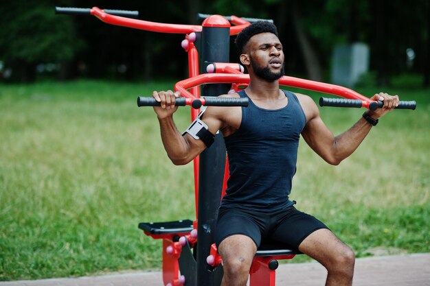 Homem esportivo de atleta masculino afro-americano com capa de braço esportivo para celular fazendo exercícios nos simuladores de treino de rua