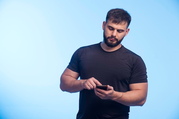 Homem esportivo de camisa preta segurando o telefone e mandando mensagens de texto