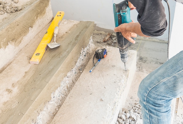 Homem está trabalhando com reforçar a modificação da estrutura da escada de concreto usando broca de mão