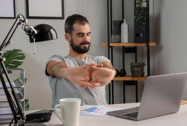 Homem esticando os braços enquanto trabalha em casa