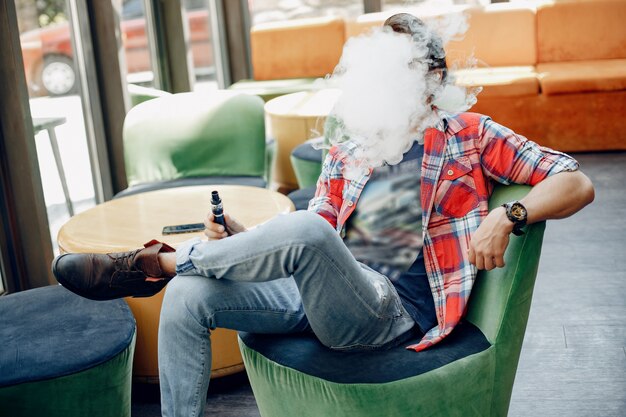 Homem estiloso e elegante, sentado em um café com vape