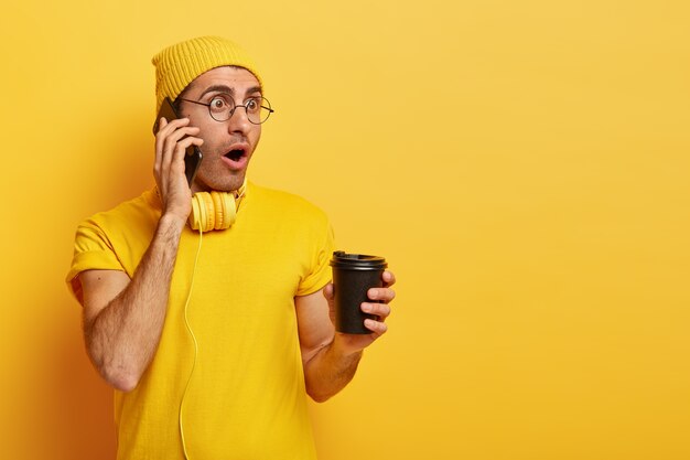 Homem estupefato conversa ao telefone, chocado com as últimas notícias, usa camiseta casual