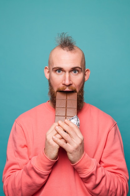 Homem europeu barbudo em pêssego casual isolado, mordendo chocolate