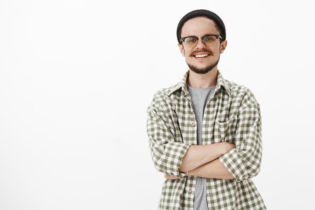 Homem europeu bonito, hábil e inteligente com gorro preto e camisa verde xadrez, sorrindo com expressão autoconfiante e realizada, sorrindo amplamente e satisfeito com o trabalho bem feito