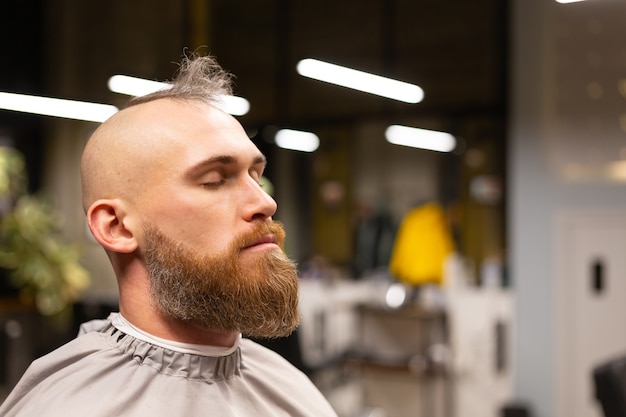 Homem europeu brutal com barba cortada em uma barbearia