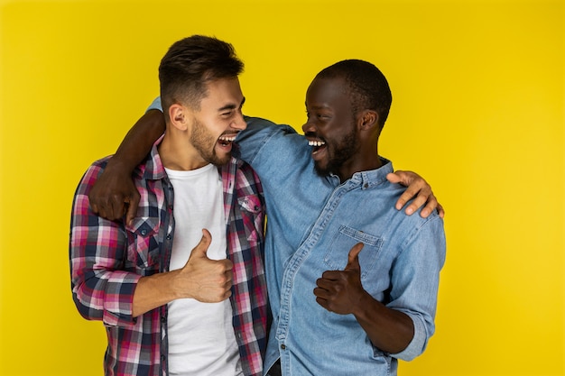 Homem europeu e africano, sorrindo e mostrando o polegar para o outro