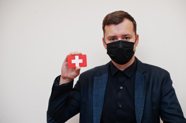 Homem europeu usa preto formal e protege máscara facial segura cartão de bandeira da Suíça isolado em fundo branco Europa coronavírus Covid país conceito