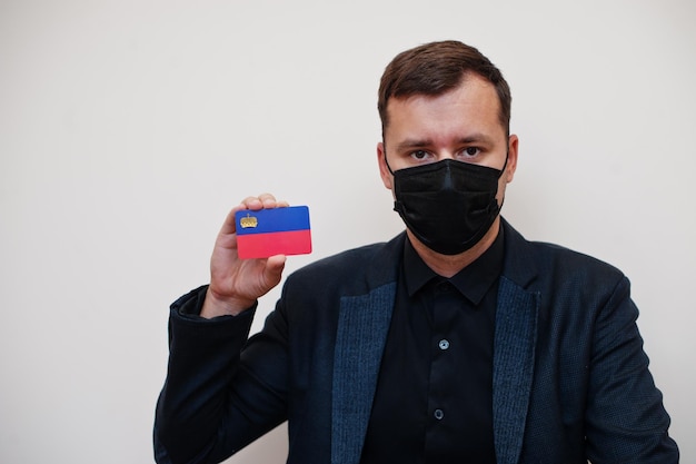 Homem europeu usa preto formal e protege máscara facial segura cartão de bandeira de Liechtenstein isolado em fundo branco Europa coronavírus Covid conceito de país