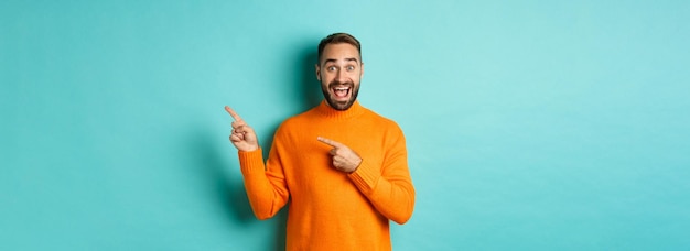 Foto grátis homem excitado fazendo um anúncio apontando os dedos para o seu logotipo sobre o fundo turquesa