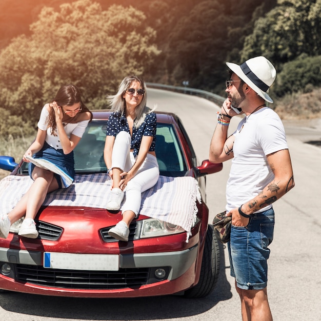 Foto grátis homem falando no celular perto dos amigos relaxantes no carro