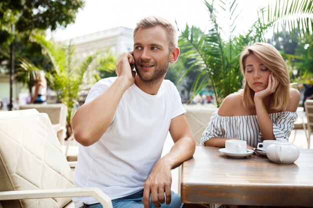 Homem falando no telefone enquanto sua namorada está entediada.