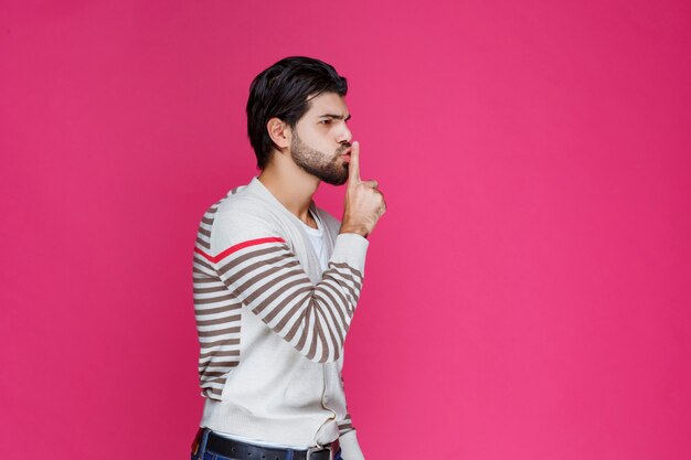 Homem fazendo arma ou sinal de mão de silêncio de perfil.