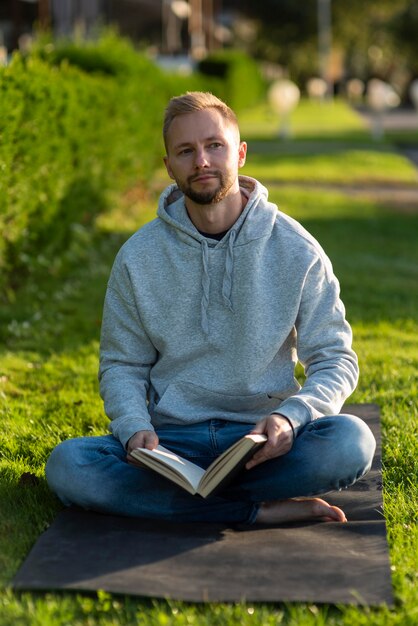 Homem fazendo posição de lótus enquanto segura um livro