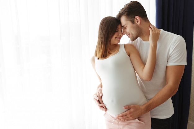 Homem feliz abraçar sua adorável esposa grávida dentro de casa em casa