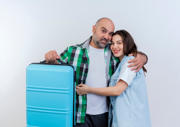 Homem feliz casal de viajantes adultos segurando uma mala e se abraçando, olhando