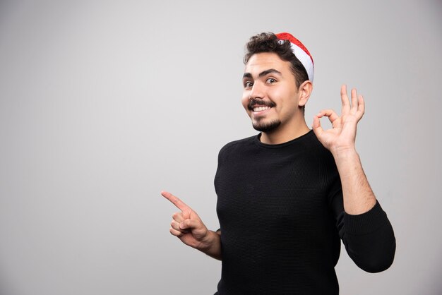 Homem feliz com chapéu de Papai Noel, mostrando o gesto de ok.