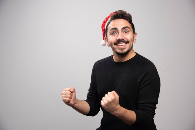 Homem feliz com chapéu de Papai Noel vermelho sobre uma parede cinza.