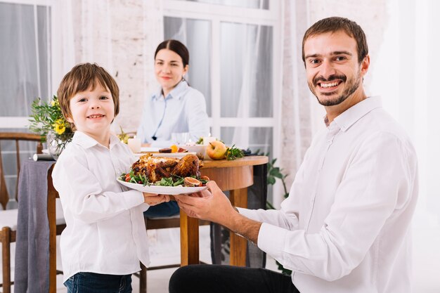 Homem feliz com o filho segurando o frango no prato