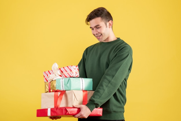 Homem feliz com suéter verde segurando presentes de pé no amarelo