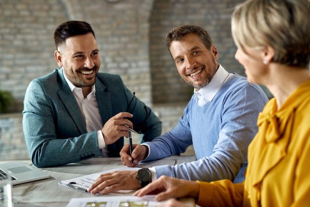 Homem feliz conversando com sua esposa enquanto assina um contrato com agente de seguros no escritório