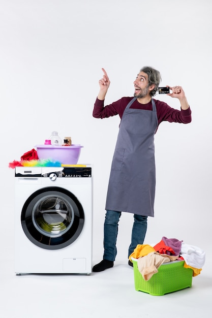 Homem feliz de vista frontal segurando um cartão em pé perto da máquina de lavar em fundo branco isolado