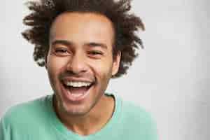 Foto grátis homem feliz radiante com pele escura e penteado espesso, sorri para a câmera e expressa emoções positivas