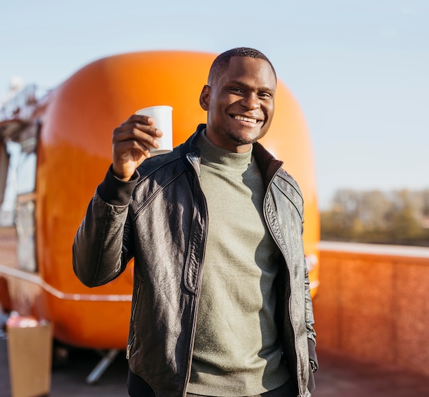 Homem feliz segurando a xícara de café na frente do caminhão de comida