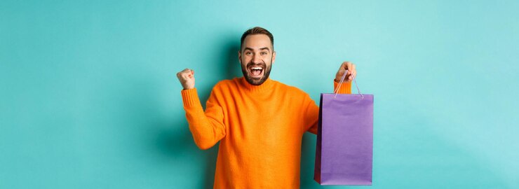 Foto grátis homem feliz segurando sacola de compras roxa e regozijando-se com desconto e comemorando em pé sobre turqu