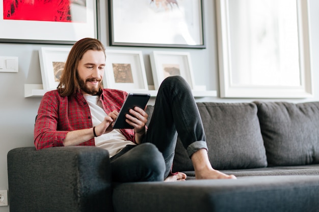 Homem feliz sentado no sofá e usando o tablet em casa