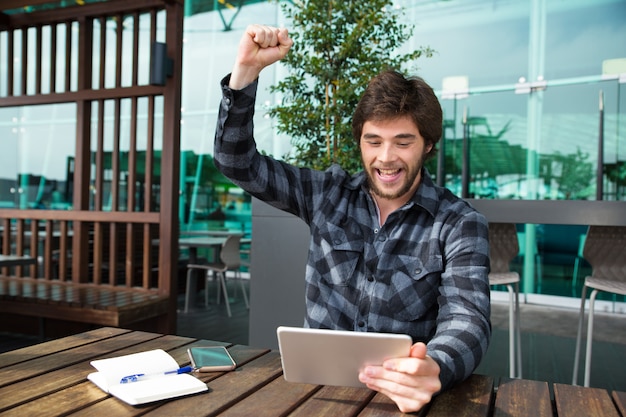 Foto grátis homem feliz usando tablet e comemorando a realização no café