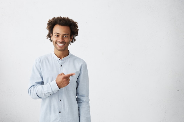 homem feliz vestido com uma camisa branca apontando para uma parede em branco