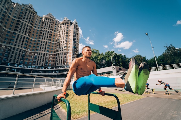 Foto grátis homem forte e musculoso fazendo exercícios em barras desiguais no ginásio de rua ao ar livre. conceito de estilo de vida de treino.